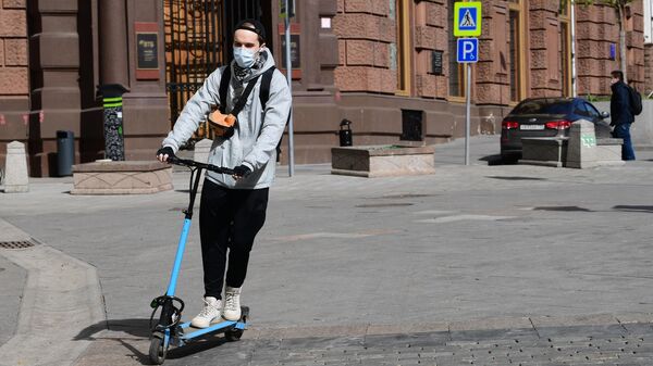 Молодой человек в защитной маске на самокате на улице Кузнецкий мост в Москве Молодой человек в защитной маске на самокате на улице Кузнецкий мост в Москве