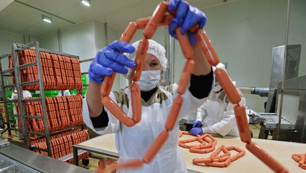Рабочий упаковывает продукцию на фабрике мясной гастрономии. Архивное фото Рабочий упаковывает продукцию на фабрике мясной гастрономии. Архивное фото