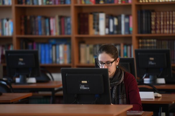 Девушка сидит за компьютером в библиотеке Девушка сидит за компьютером в библиотеке