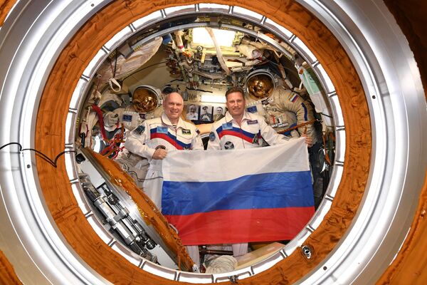 Российские космонавты Олег Артемьев и Сергей Прокопьев с флагом страны в День Государственного флага на борту МКС Российские космонавты Олег Артемьев и Сергей Прокопьев с флагом страны в День Государственного флага на борту МКС