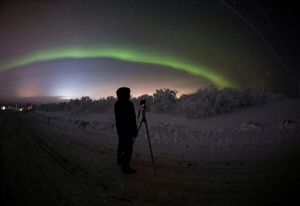 Мужчина фотографирует северное сияние на трассе Серебрянка в Мурманской области Мужчина фотографирует северное сияние на трассе Серебрянка в Мурманской области